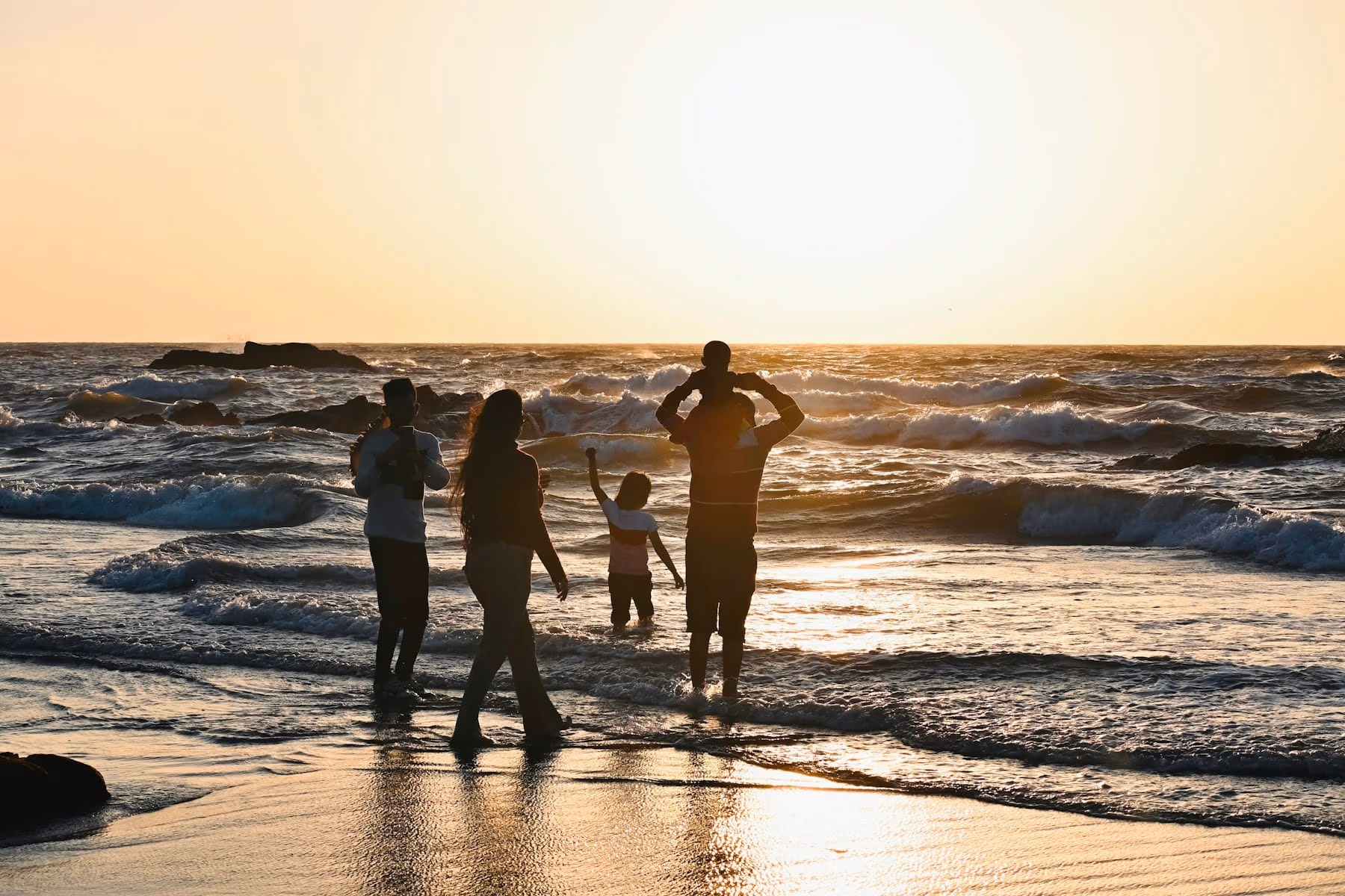 Famille les pieds dans les vagues de l'océan au coucher du soleil, un enfant sur les épaules de son père