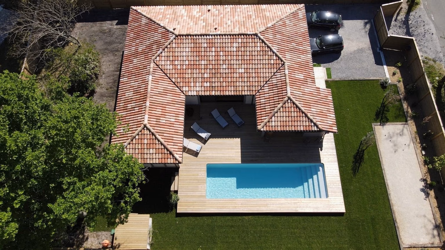 Vue aérienne de la maison de plain-pied en L construite par Landes Habitat à Moliets-et-Maâ (40) : terrasse bois, piscine et terrain de pétanque