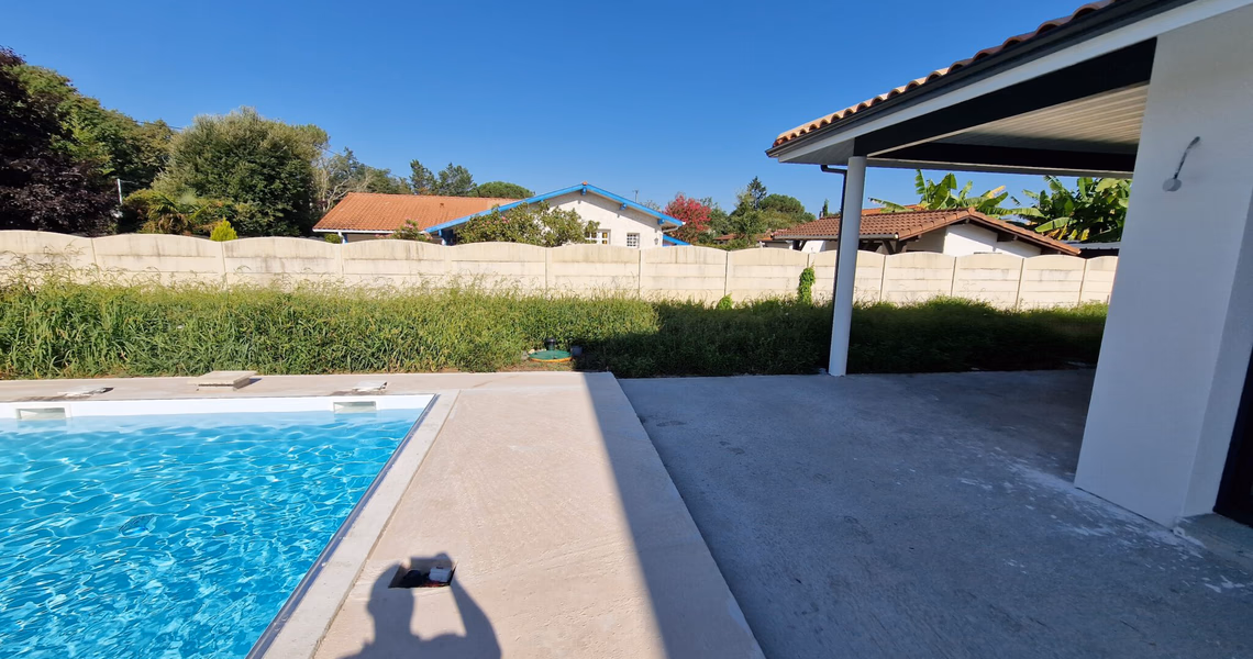 Piscine extérieure avec terrasse en béton et pool house couvert sous un ciel bleu dégagé.