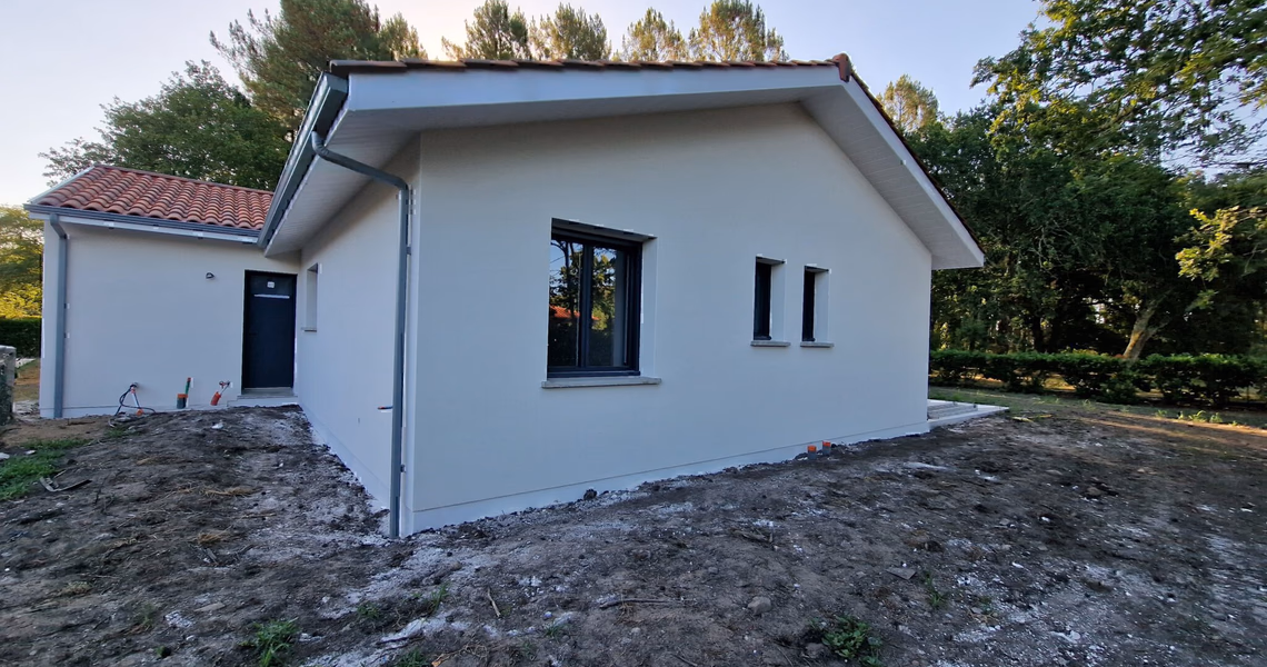 Façade latérale avec fenêtres gris anthracite, débord de toit blanc et terrain arboré à Herm