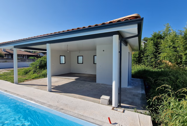 Pool house contemporain ouvert sur une piscine extérieure avec un toit en tuiles et des piliers blancs.