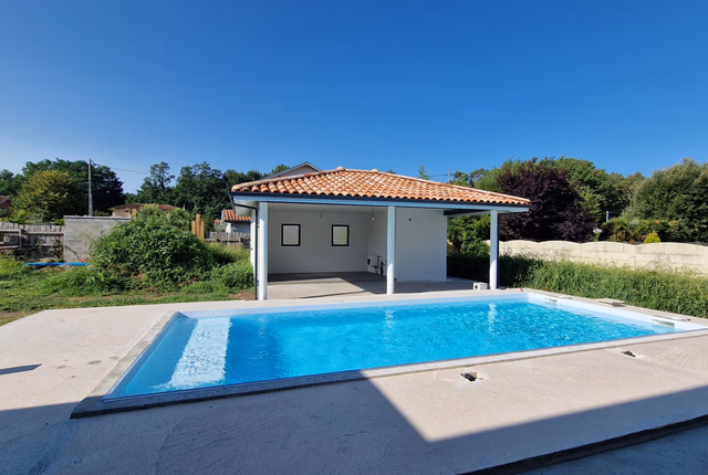 Piscine rectangulaire à l'eau bleue devant un pool-house couvert avec toiture en tuiles canal.