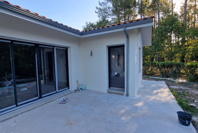 Baie vitrée coulissante en aluminium gris anthracite donnant sur la terrasse au cœur de la pinède à Herm