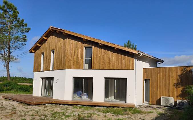 Maison moderne à deux étages avec crépi blanc, bardage bois vertical, grandes baies vitrées et terrasse en bois
