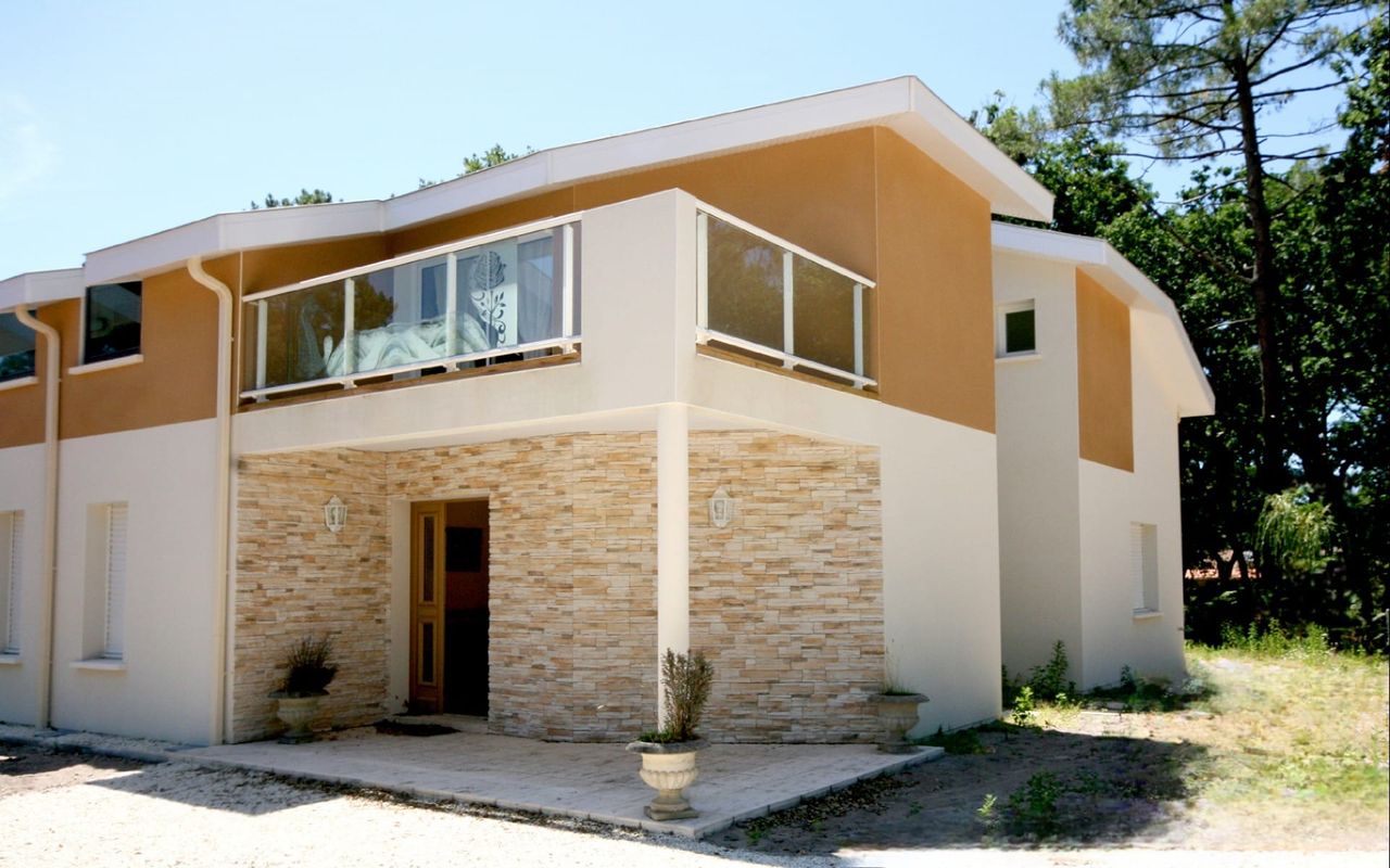 Entrée de maison R+1 contemporaine à Vieux-Boucau avec parement pierre, garde-corps vitré et enduit deux tons – Réalisation Landes Habitat