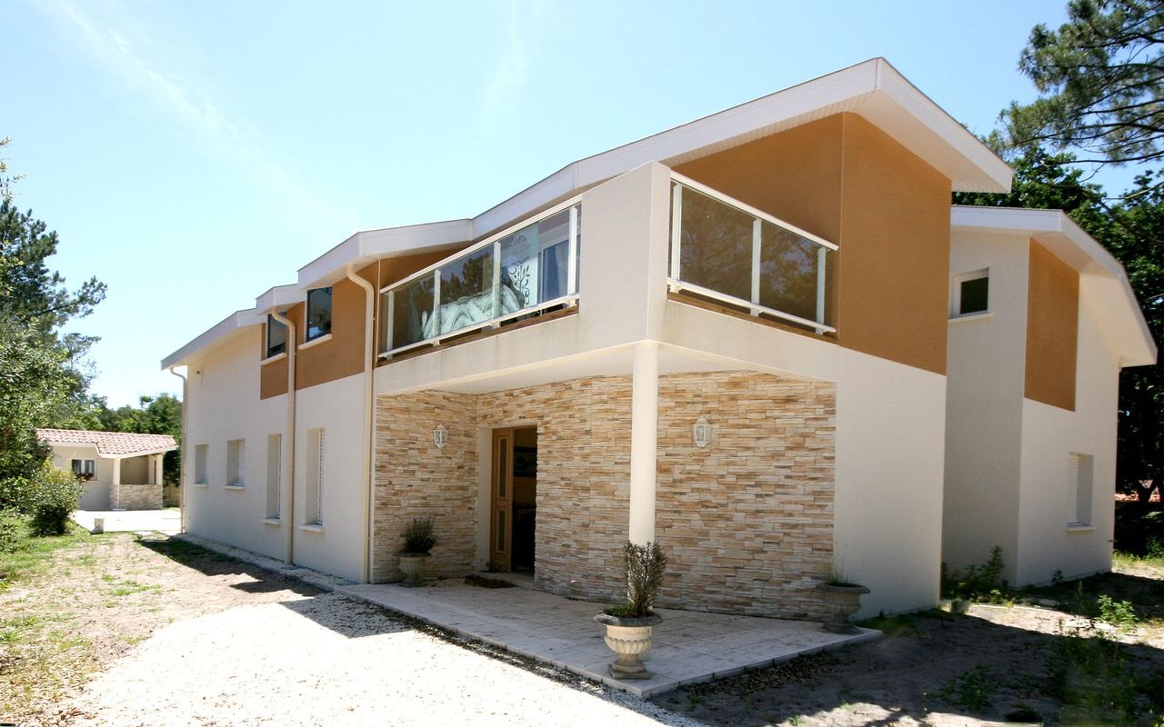 Façade latérale de maison contemporaine à Vieux-Boucau avec parement pierre, garde-corps vitré et accès paysager – Construction Landes Habitat