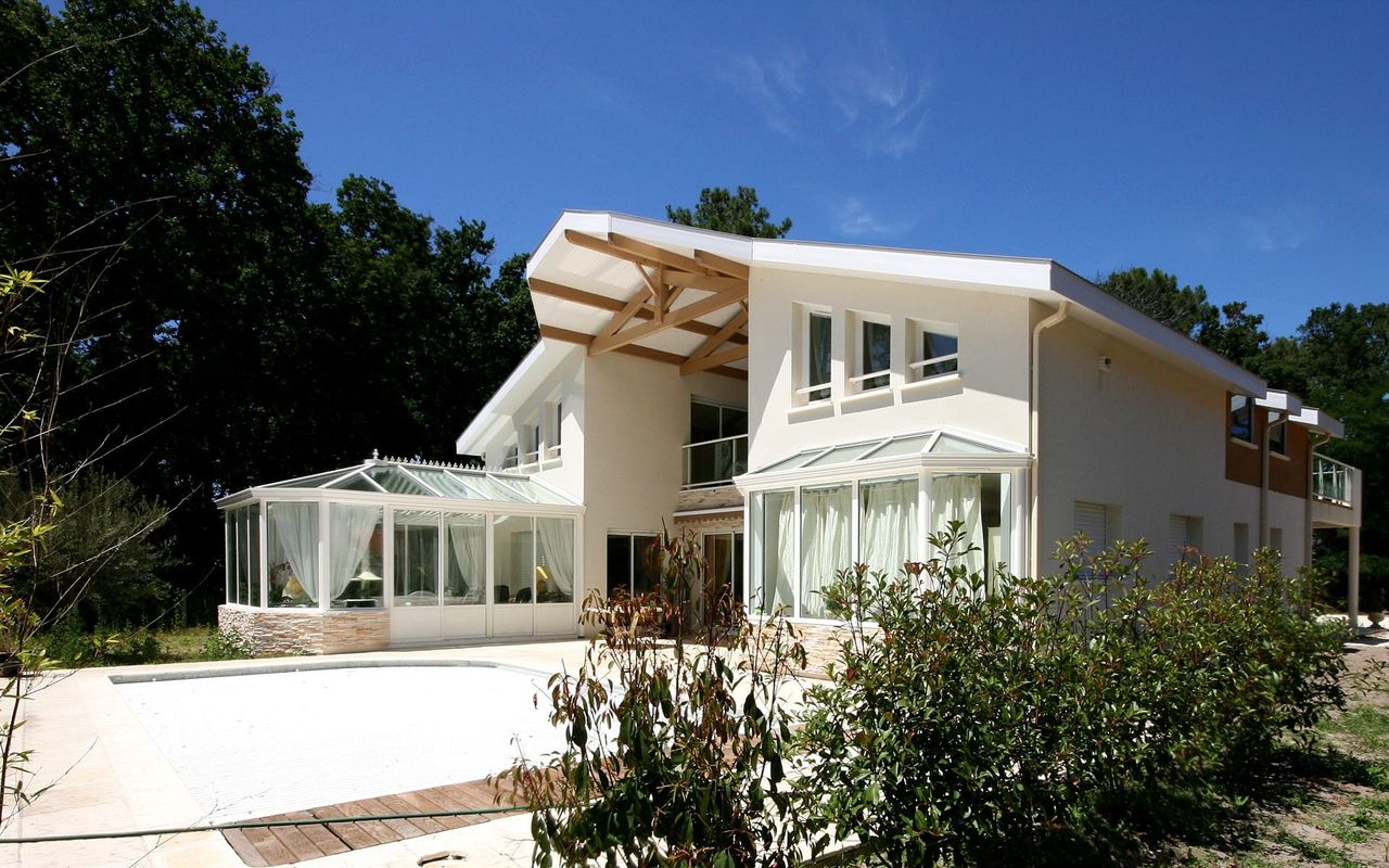 vue-arriere-maison-vieux-boucau-charpente-piscine-veranda-landes-habitat.jpg" alt="Vue arrière de la maison contemporaine à Vieux-Boucau avec vérandas, charpente apparente en bois, piscine couverte et grandes baies vitrées – Landes Habitat