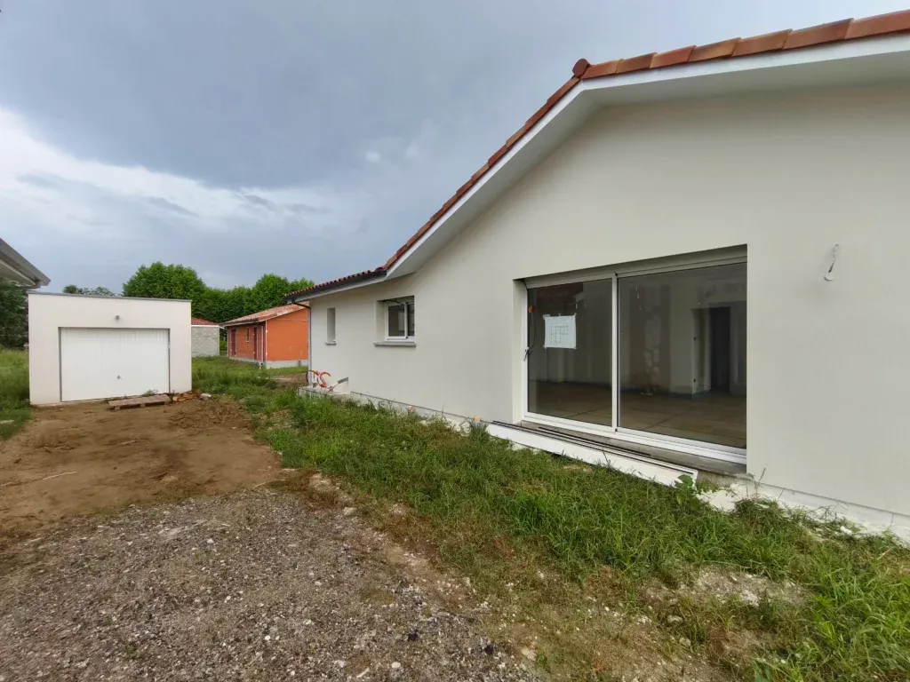 Grande baie vitrée coulissante en aluminium sur la façade arrière d'une maison contemporaine avec garage indépendant.
