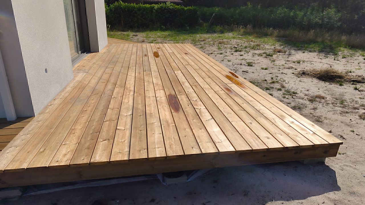 Grande terrasse en bois faite de planches attenante à une maison blanche