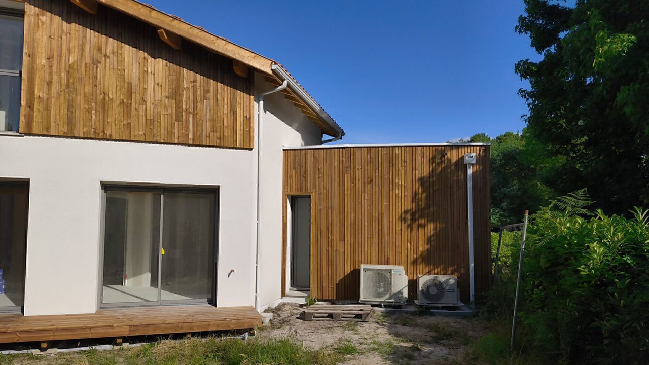 Maison moderne avec bardage bois, crépi blanc et deux unités de climatisation extérieures
