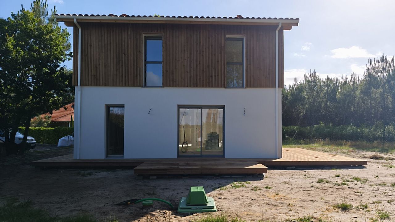 Maison moderne à deux étages avec bardage en bois à l'étage, rez-de-chaussée blanc et terrasse en bois