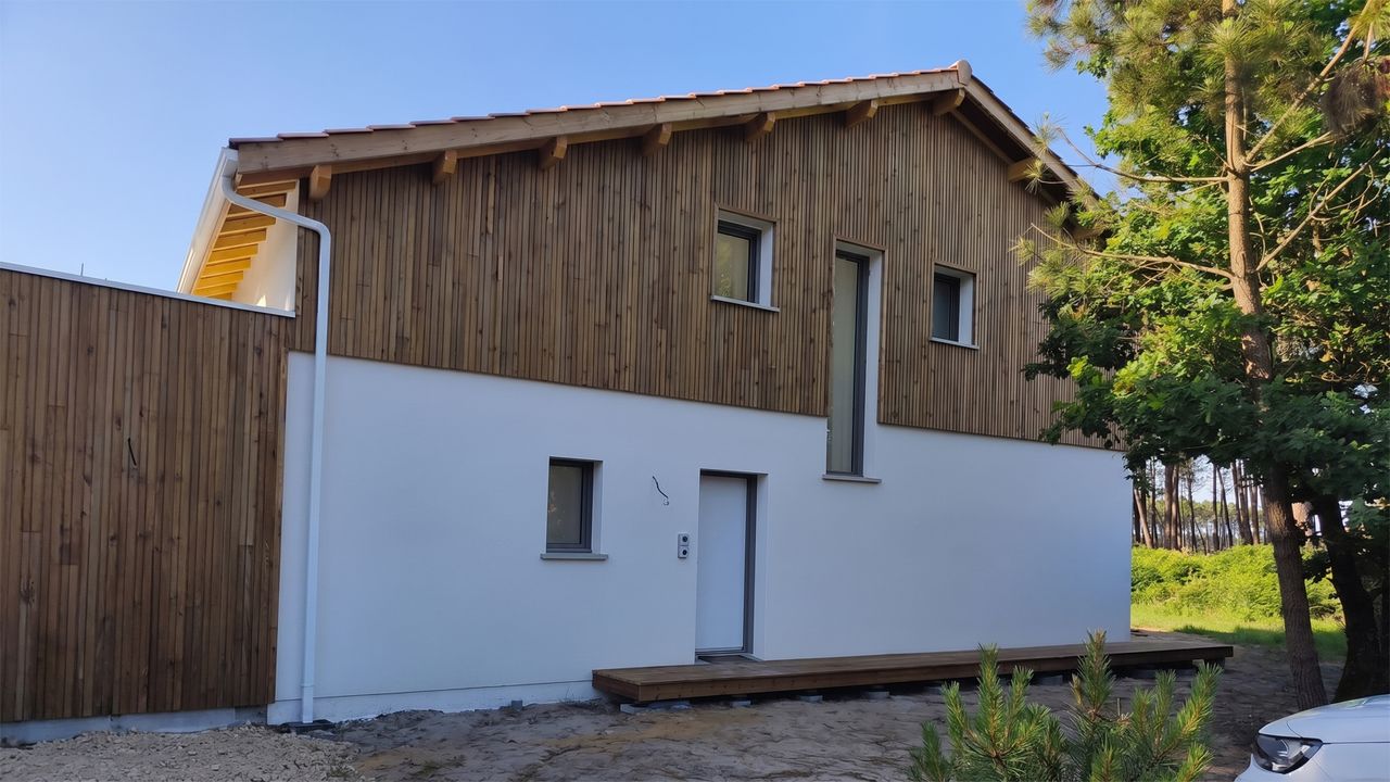 Maison moderne avec rez-de-chaussée blanc et bardage bois vertical à l'étage, entourée de pins