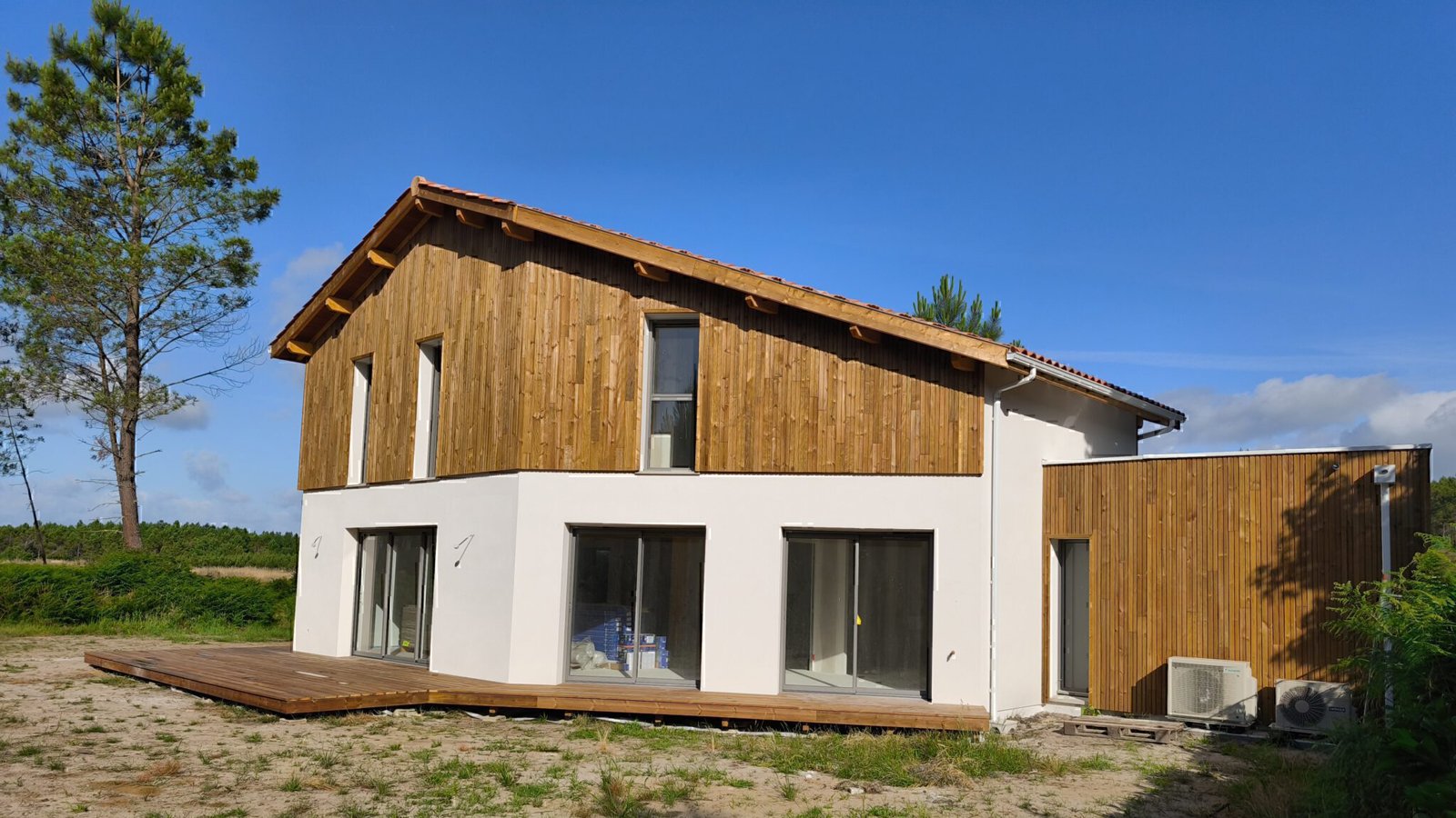 Maison moderne à deux étages avec crépi blanc, bardage bois vertical, grandes baies vitrées et terrasse en bois